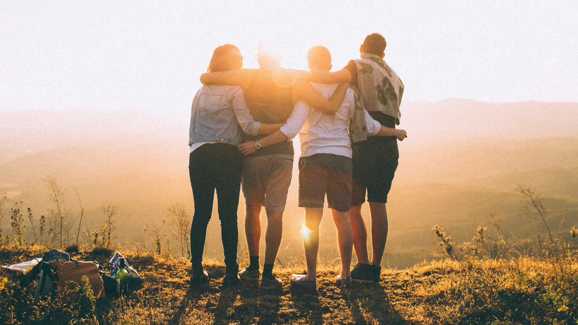 Quatre jeunes contemplent ensemble le coucher de soleil depuis un point de vue panoramique.